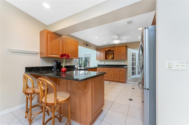 kitchen with sink, stainless steel fridge, dark stone countertops, light tile patterned flooring, and kitchen peninsula