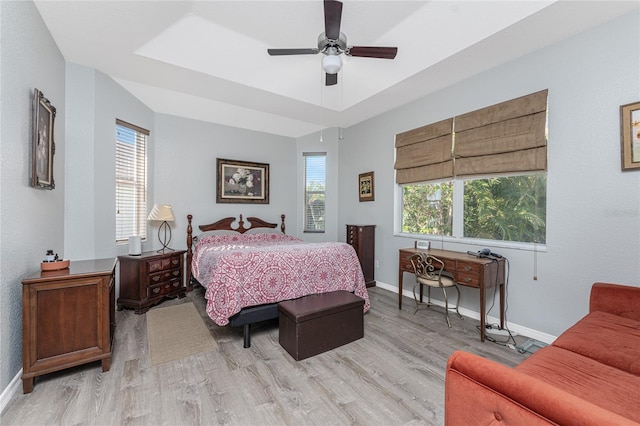 bedroom featuring multiple windows, a tray ceiling, ceiling fan, and light hardwood / wood-style flooring