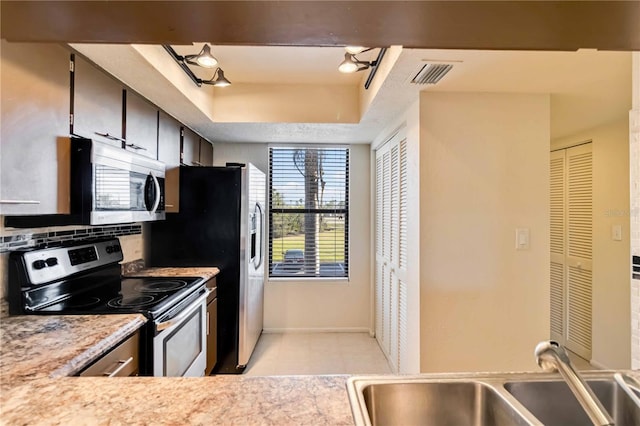 kitchen with dark brown cabinetry, sink, appliances with stainless steel finishes, a tray ceiling, and decorative backsplash