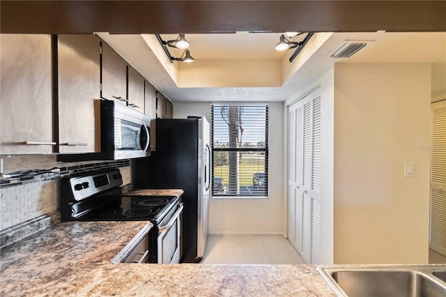 kitchen with appliances with stainless steel finishes, a raised ceiling, and decorative backsplash