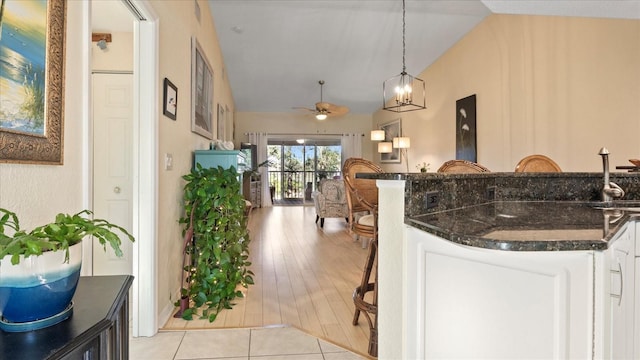 kitchen featuring lofted ceiling, dark stone countertops, white cabinets, hanging light fixtures, and ceiling fan