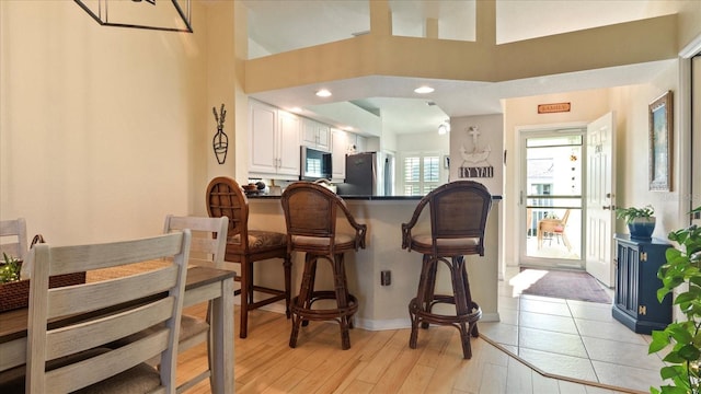 kitchen with a breakfast bar, white cabinetry, light hardwood / wood-style flooring, appliances with stainless steel finishes, and kitchen peninsula