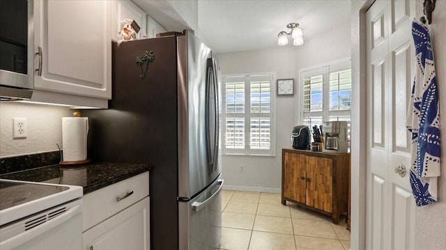 kitchen with stainless steel refrigerator, white cabinetry, dark stone countertops, light tile patterned floors, and electric range