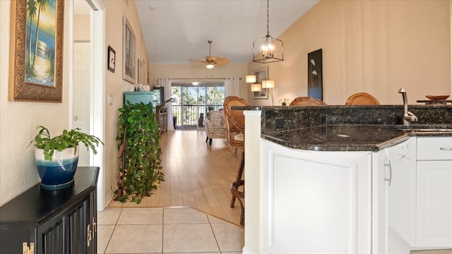 kitchen with light tile patterned flooring, sink, hanging light fixtures, dark stone countertops, and white cabinets