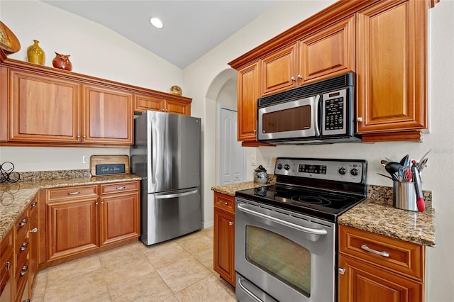 kitchen featuring light tile patterned flooring, appliances with stainless steel finishes, light stone countertops, and vaulted ceiling