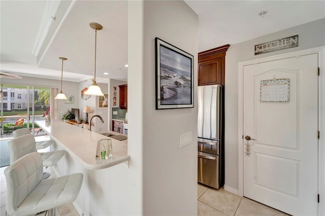 kitchen with sink, light tile patterned floors, stainless steel refrigerator, a kitchen bar, and decorative light fixtures