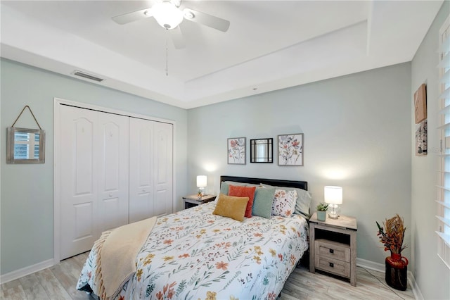 bedroom featuring ceiling fan, a tray ceiling, light wood-type flooring, and a closet