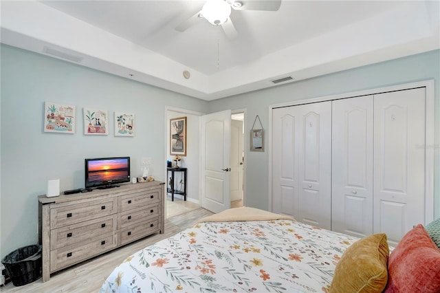 bedroom featuring a raised ceiling, light hardwood / wood-style flooring, ceiling fan, and a closet