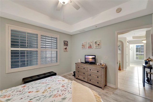 bedroom with ceiling fan, a raised ceiling, and light hardwood / wood-style flooring