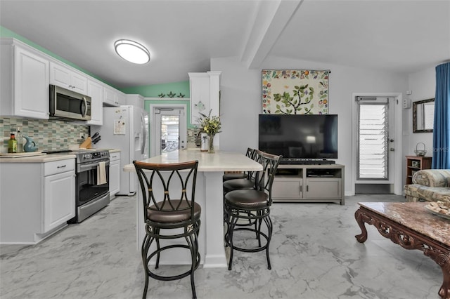 kitchen featuring a breakfast bar, appliances with stainless steel finishes, kitchen peninsula, decorative backsplash, and white cabinets