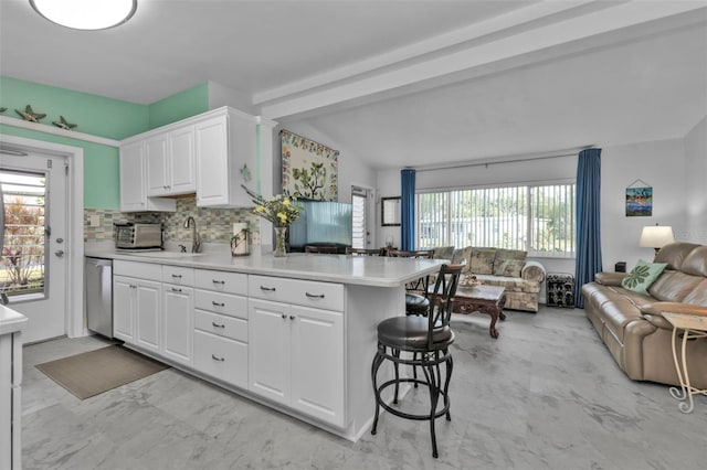 kitchen featuring stainless steel dishwasher, a kitchen breakfast bar, kitchen peninsula, decorative backsplash, and white cabinets