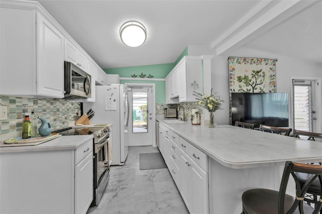 kitchen featuring white cabinetry, vaulted ceiling, appliances with stainless steel finishes, a kitchen breakfast bar, and kitchen peninsula