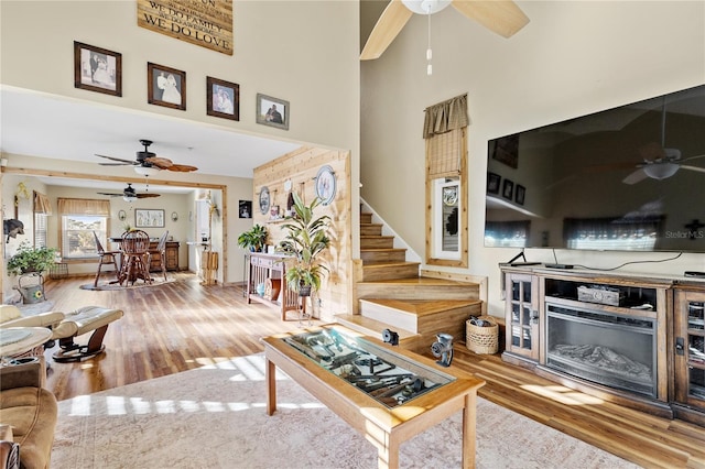 living room featuring hardwood / wood-style flooring, ceiling fan, a towering ceiling, and a fireplace