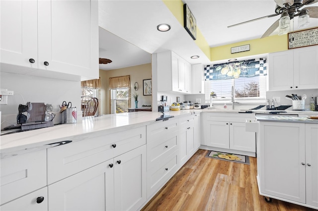 kitchen with ceiling fan, light hardwood / wood-style floors, light stone countertops, white cabinets, and kitchen peninsula