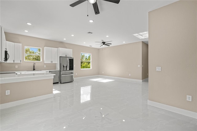 kitchen featuring stainless steel appliances, a sink, white cabinets, open floor plan, and light countertops