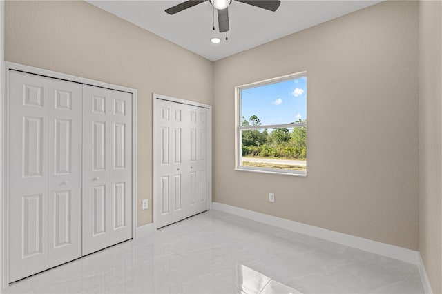 unfurnished bedroom featuring ceiling fan, baseboards, and two closets