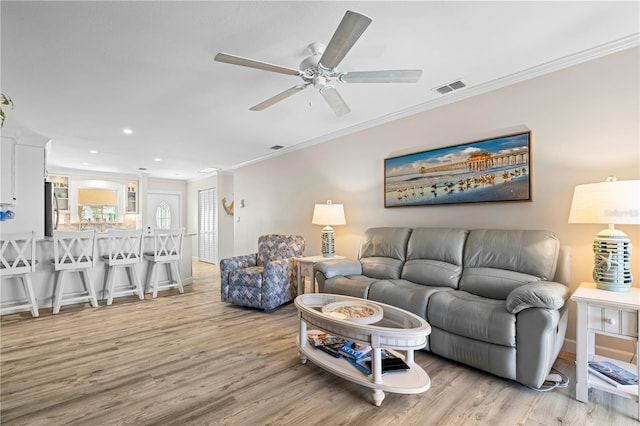 living room featuring ceiling fan, ornamental molding, and light wood-type flooring