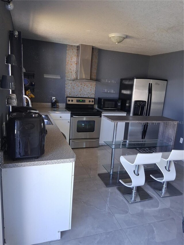 3380 Maple Ter, Port Charlotte, FL 33952 - kitchen featuring wall chimney range hood, white cabinets, appliances with stainless steel finishes, and a textured ceiling