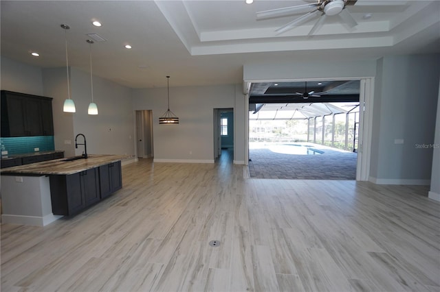 kitchen featuring pendant lighting, dark stone counters, a tray ceiling, and sink