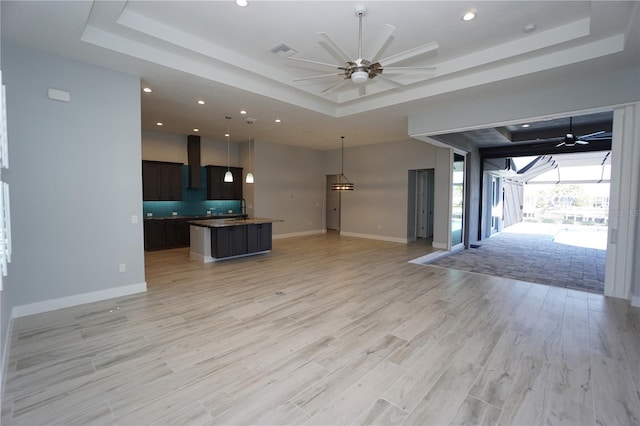 unfurnished living room featuring ceiling fan, a raised ceiling, and light wood-type flooring