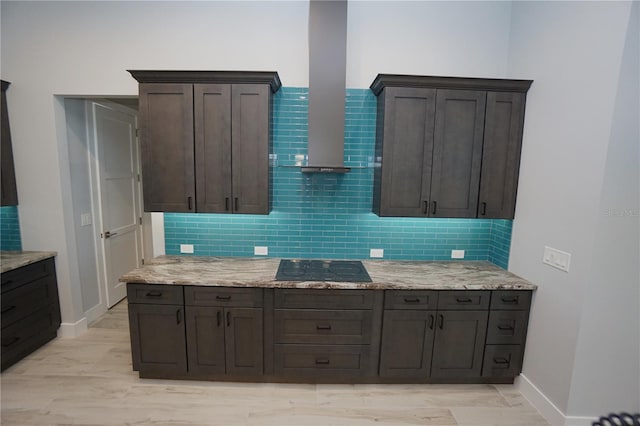 kitchen featuring backsplash, dark brown cabinetry, light stone countertops, wall chimney range hood, and black electric cooktop