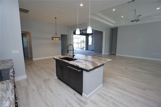 kitchen featuring decorative light fixtures, black dishwasher, sink, light stone counters, and a center island with sink