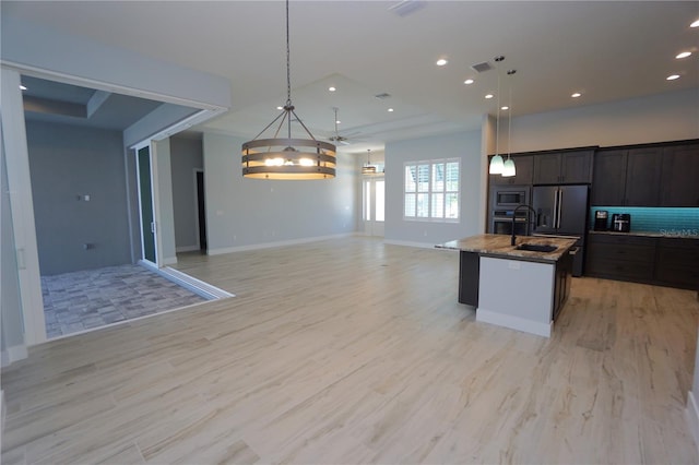 kitchen with stone counters, an island with sink, stainless steel microwave, and decorative light fixtures