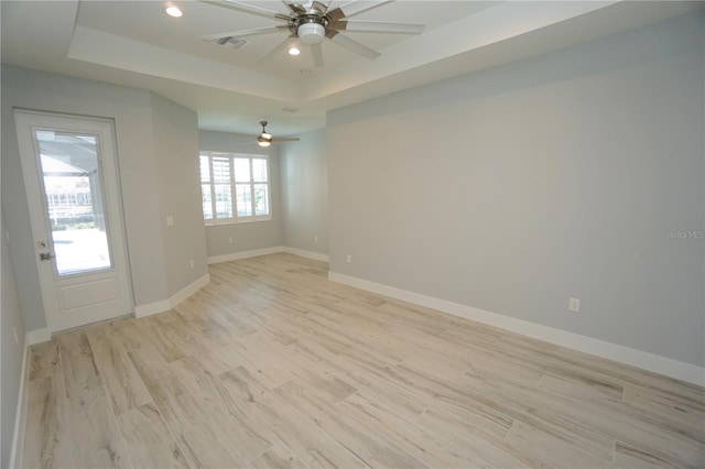 spare room with a tray ceiling, light hardwood / wood-style flooring, and ceiling fan