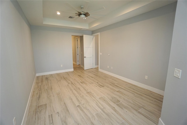 spare room with a raised ceiling, ceiling fan, and light hardwood / wood-style flooring