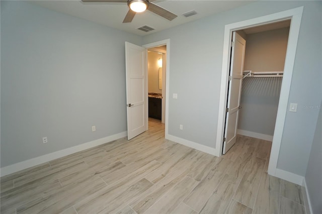 unfurnished bedroom with ceiling fan, a walk in closet, light hardwood / wood-style floors, and a closet