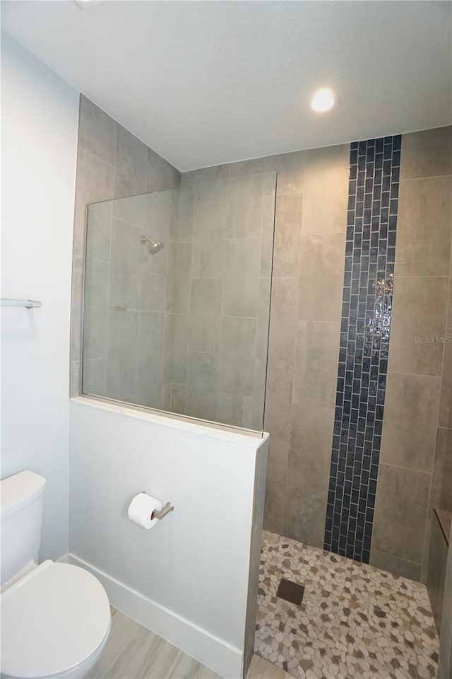 bathroom featuring a tile shower, wood-type flooring, and toilet