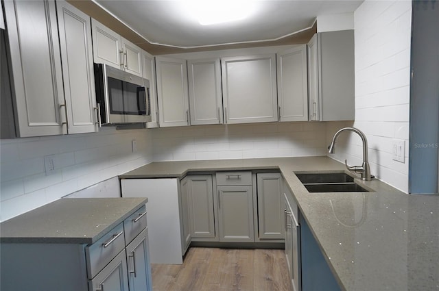 kitchen with tasteful backsplash, dark stone counters, sink, and light wood-type flooring