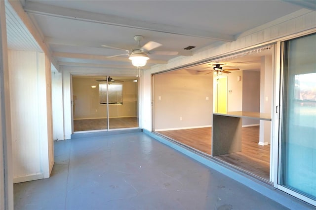 spare room featuring beamed ceiling, ceiling fan, and concrete floors