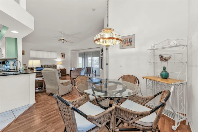 dining area featuring lofted ceiling, sink, ceiling fan with notable chandelier, and light wood-type flooring