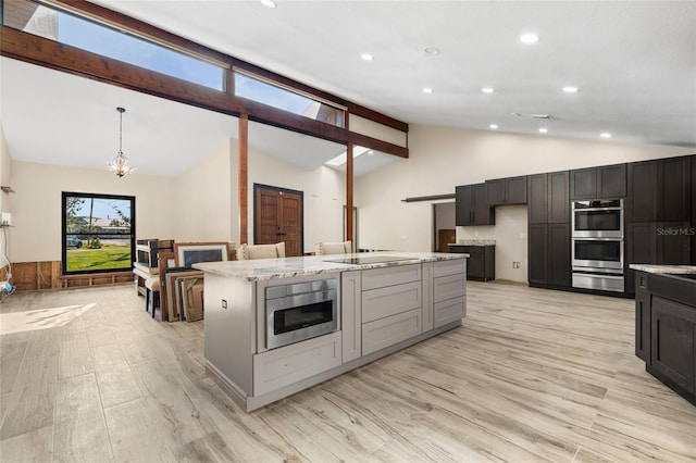 kitchen featuring hanging light fixtures, light hardwood / wood-style flooring, double oven, light stone countertops, and a kitchen island with sink