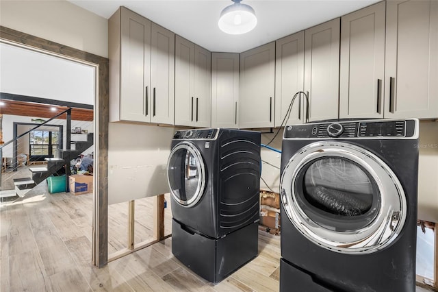 clothes washing area featuring cabinets, washing machine and dryer, and light hardwood / wood-style flooring