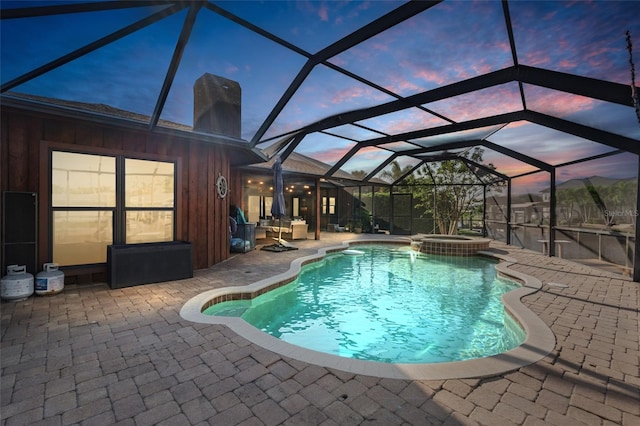 pool at dusk with an in ground hot tub, a patio area, and glass enclosure