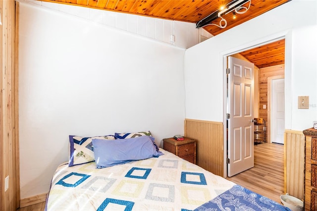 bedroom with lofted ceiling, wood ceiling, light hardwood / wood-style flooring, track lighting, and wooden walls