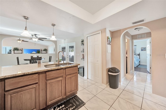 kitchen with sink, light tile patterned floors, hanging light fixtures, light stone counters, and french doors