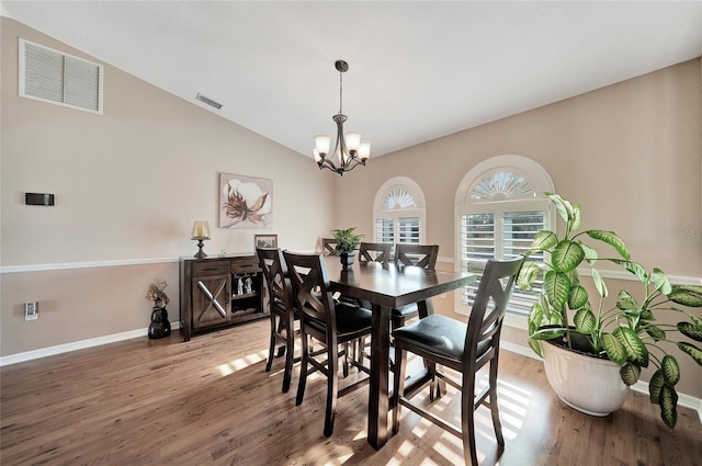 dining space with hardwood / wood-style flooring, vaulted ceiling, and a chandelier