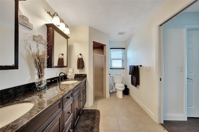 bathroom featuring tile patterned flooring, vanity, a textured ceiling, a shower with shower door, and toilet