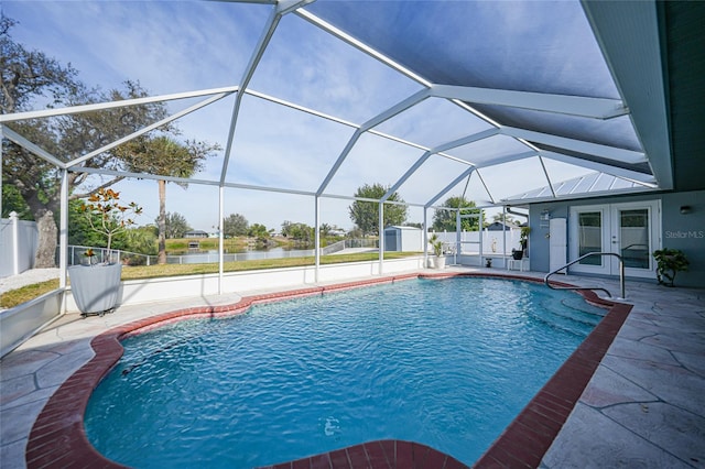 view of pool featuring a patio, glass enclosure, a shed, a water view, and french doors