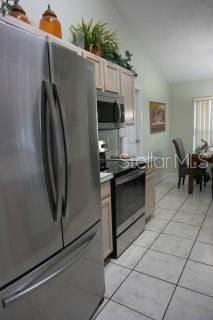 kitchen featuring stainless steel appliances, light brown cabinetry, vaulted ceiling, and light tile patterned floors