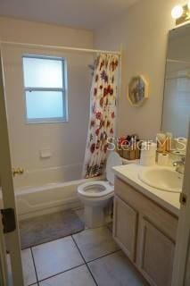 full bathroom with vanity, shower / bathtub combination with curtain, tile patterned floors, and toilet