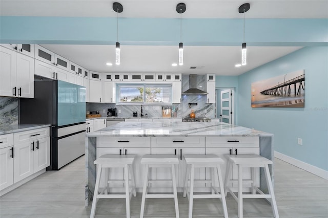 kitchen featuring a spacious island, sink, appliances with stainless steel finishes, pendant lighting, and wall chimney range hood