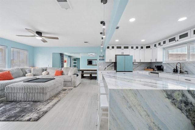 kitchen featuring refrigerator, light stone countertops, decorative backsplash, white cabinets, and decorative light fixtures