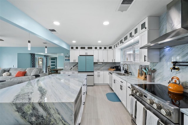 kitchen featuring wall chimney range hood, sink, appliances with stainless steel finishes, white cabinetry, and a spacious island