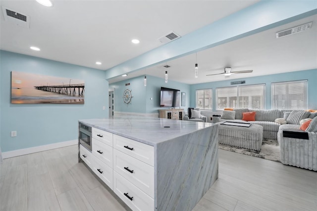 kitchen featuring ceiling fan, white cabinetry, a center island, stainless steel microwave, and light stone countertops