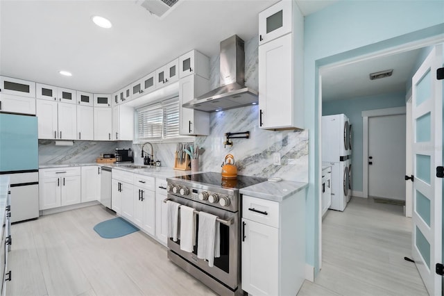 kitchen featuring stacked washer / dryer, white cabinetry, stainless steel appliances, light stone countertops, and wall chimney exhaust hood