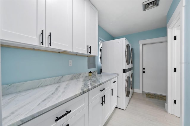 clothes washing area with cabinets, stacked washer / dryer, and light hardwood / wood-style floors